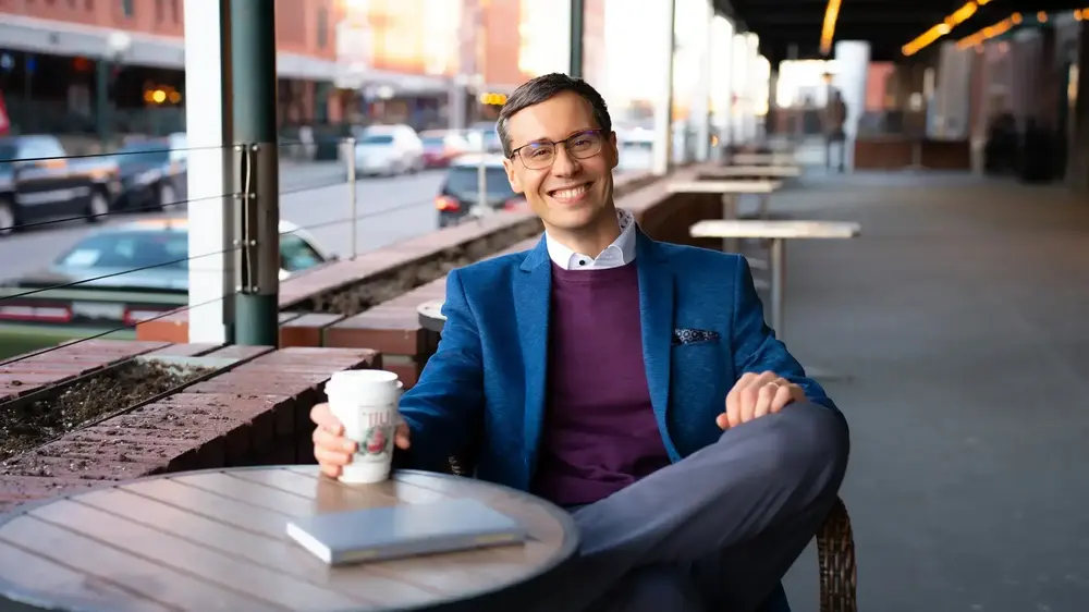 Joshua Berry at a café table, smiling, with a coffee in his hand